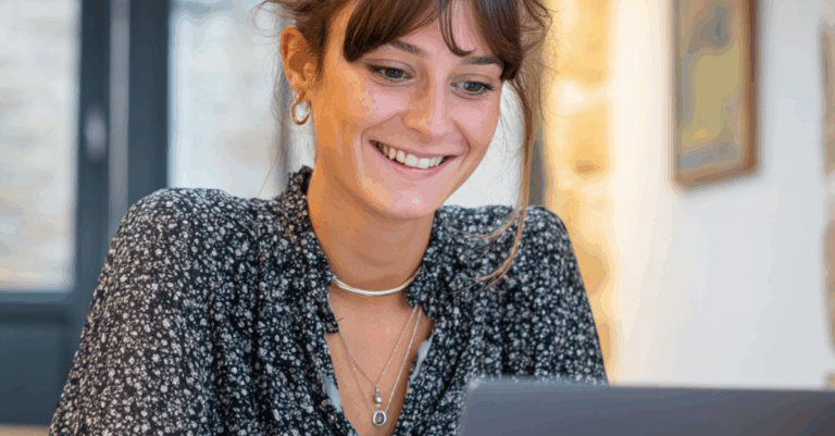 Esthéticienne souriante travaillant sur un ordinateur portable dans son institut, planifiant ses publications réseaux sociaux pour attirer de nouvelles clientes. Marketing Digital Pour Esthéticienne